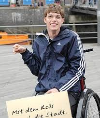 Bild Mann im Rollstuhl Schild Mit dem Rolli durch die Stadt