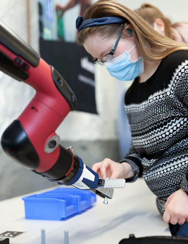 Frau mit Mundschutz arbeitet mit Roboter